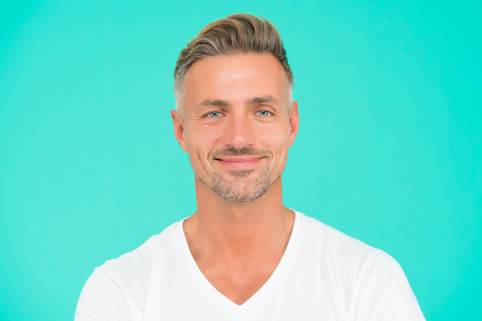 smiling guy with trendy hairstyle has colored graying hair and groomed face on turquoise background, personal care